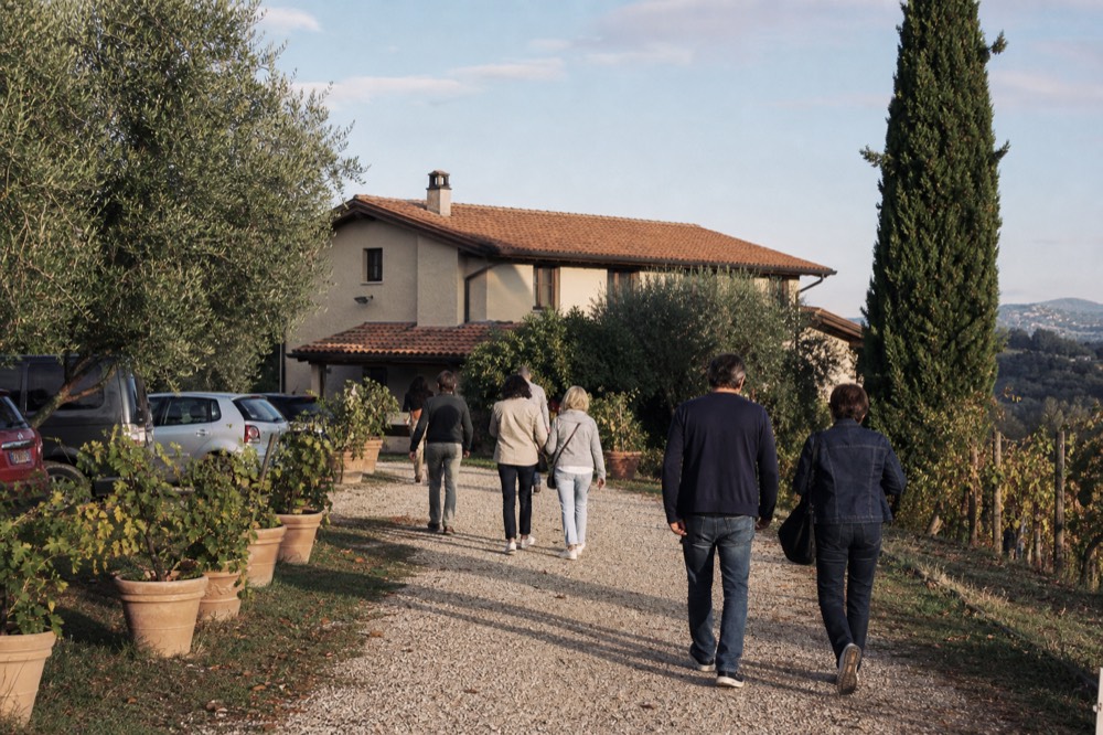 The exterior of a traditional acetaia in the Modena countryside, with a sign reading Acetaia Aperta and a group of visitors entering.