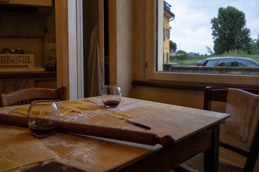 A home kitchen table set with rolled dough, a long wooden rolling pin and glasses of red wine
