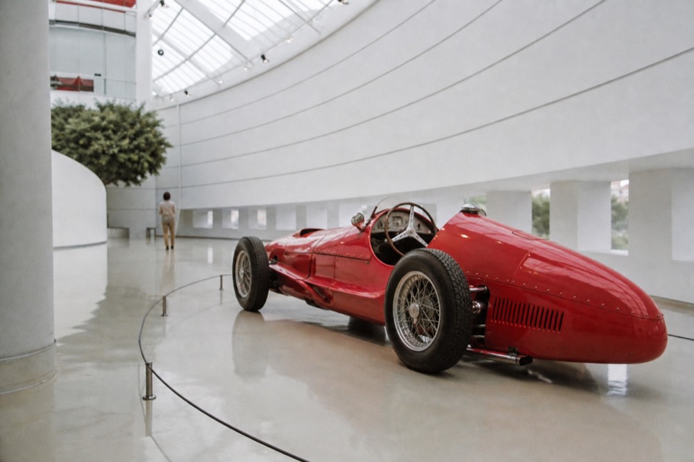 Modern museum building with curved white architecture and a red vintage racing car inside a glass hall