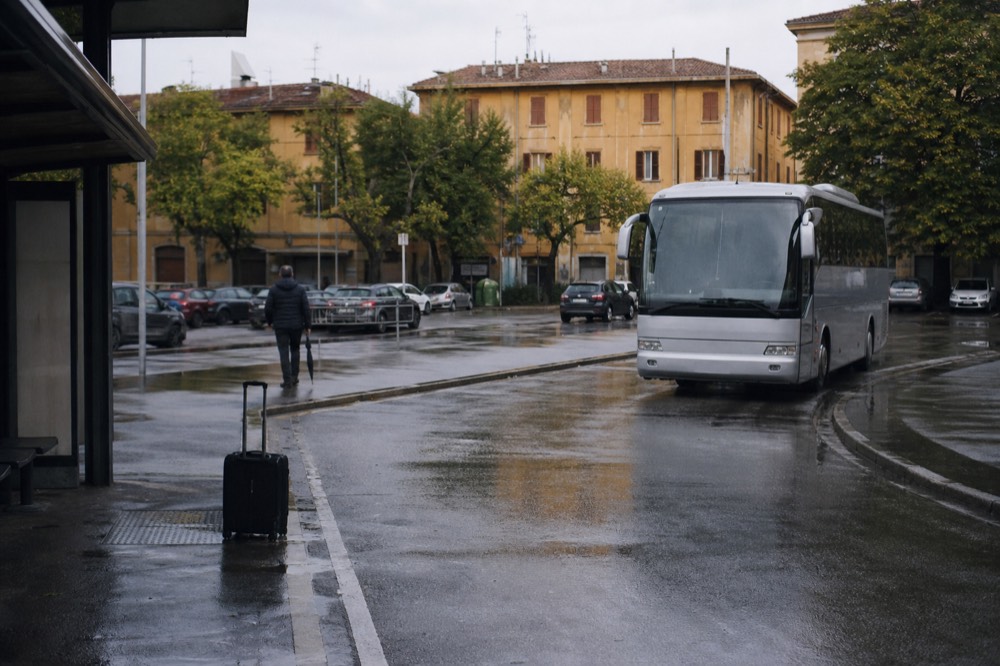 Regional bus parked at a station bay beside a modern Italian railway station entrance