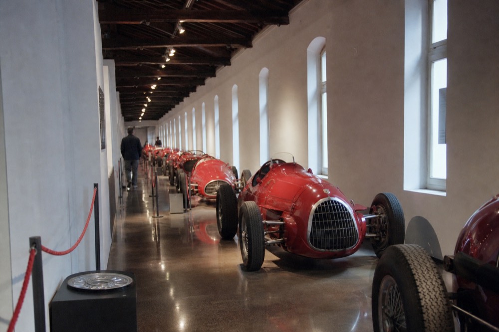 Long hallway of a car museum with polished vintage racing cars on polished floors under spotlights
