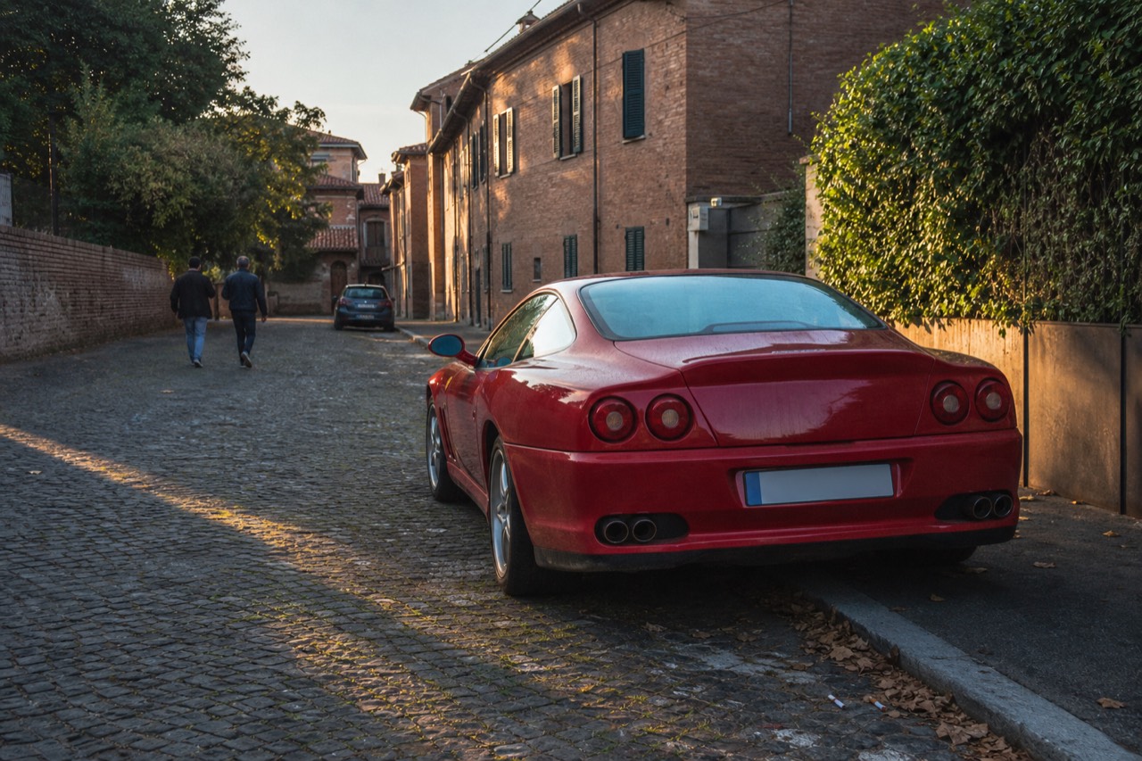 Red Ferrari sports car parked on a cobblestone street in an Italian town with old brick buildings
