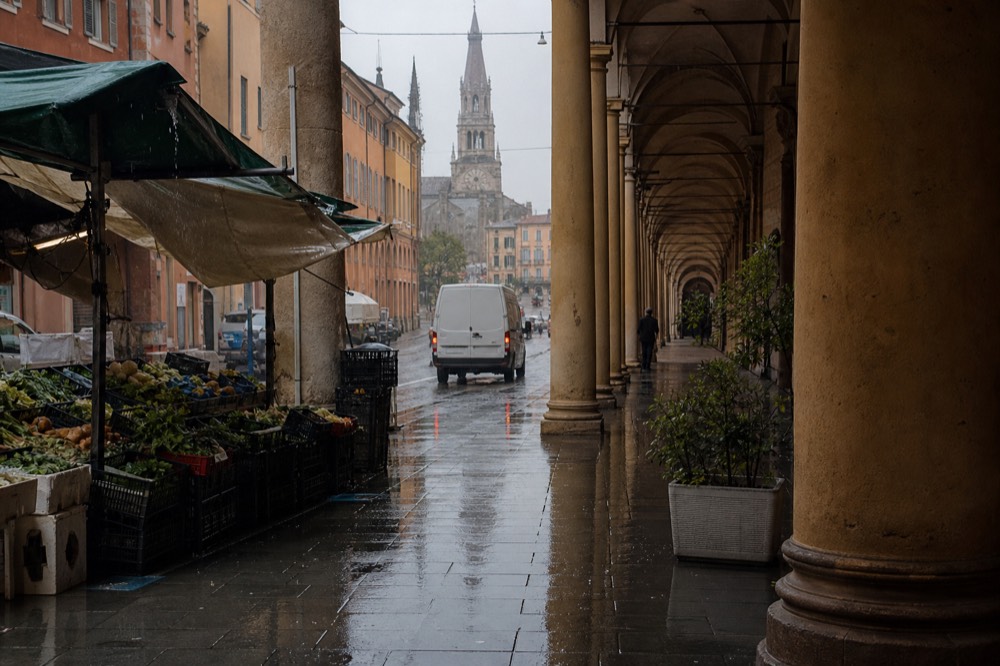 A porticoed city street with market stalls and old towers in the distance