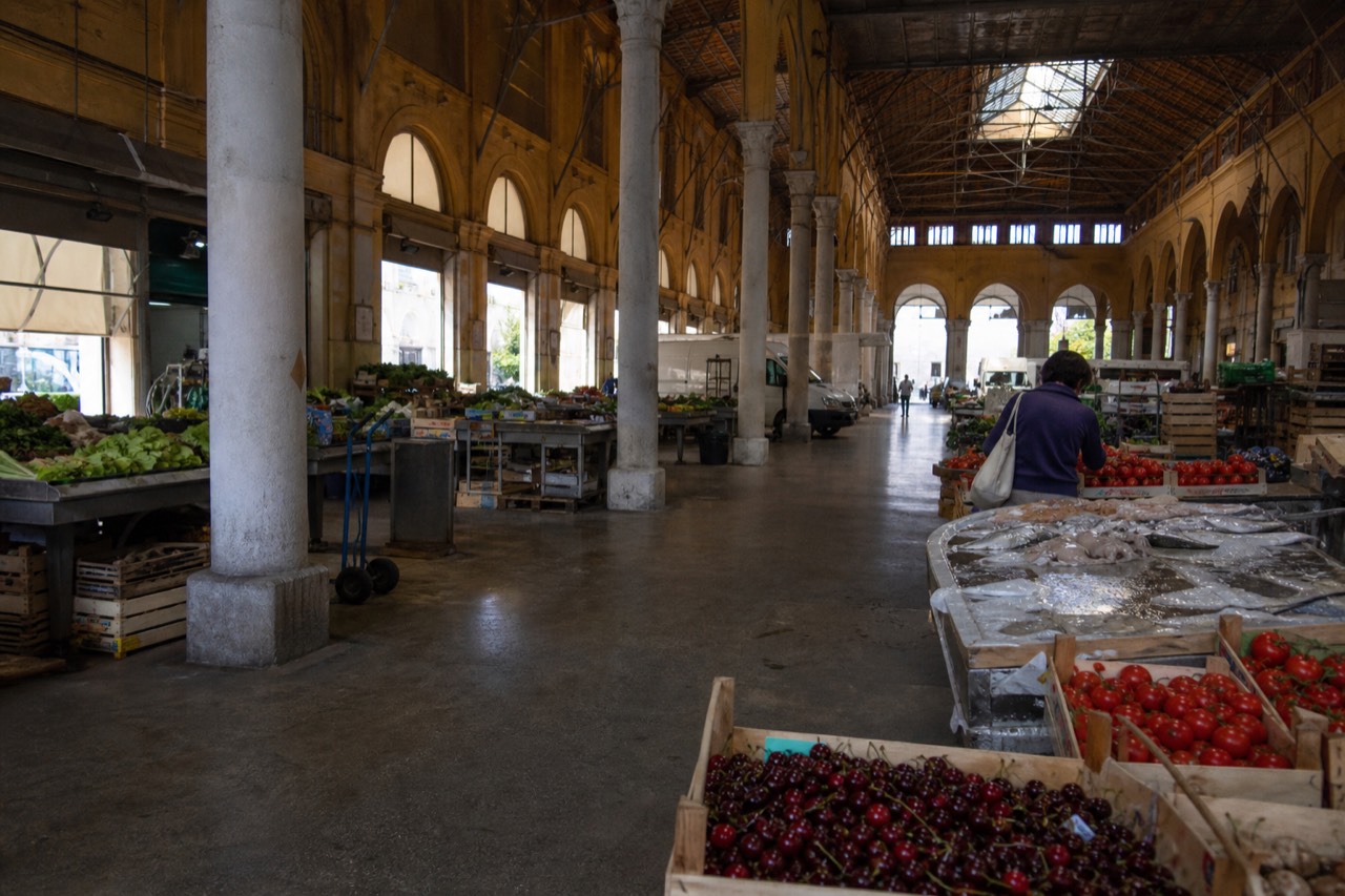 A covered market hall with produce stalls under an arched ceiling