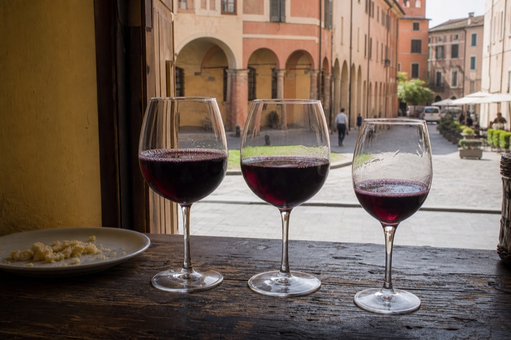 Three glasses of red Lambrusco poured side by side on a wooden tasting counter
