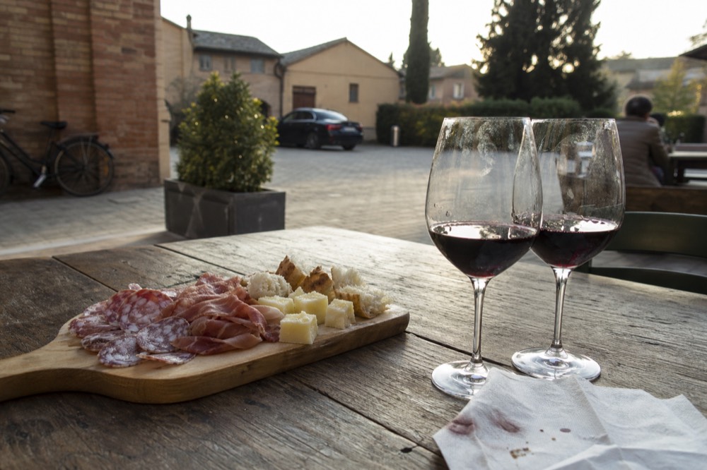 A tasting plate with cured meats, cheese and bread beside glasses of red wine