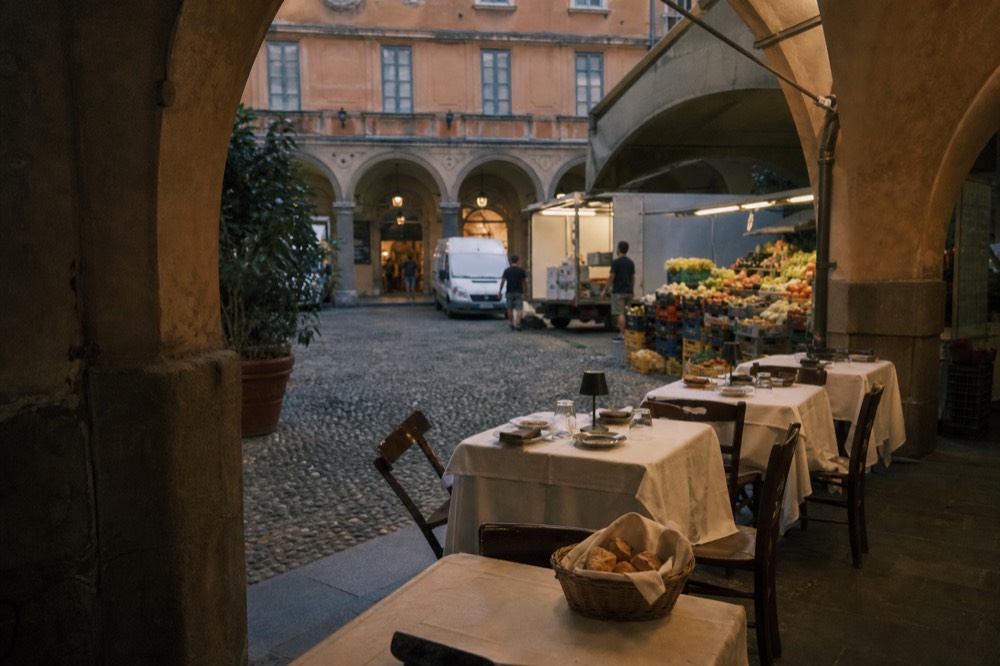 Small restaurant tables set beside a market aisle inside a covered hall