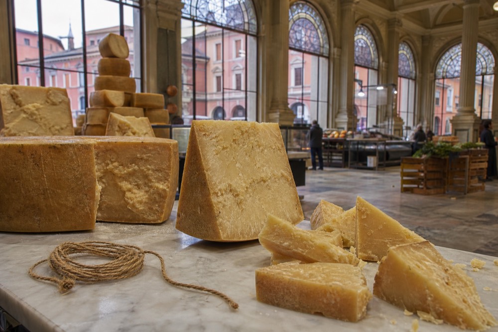 A cheese counter with whole wheels and cut wedges of aged cheese on a marble slab