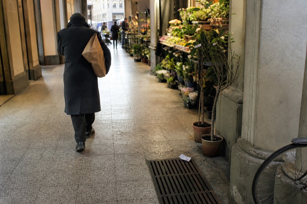 A shopper carrying a paper-wrapped parcel past market stalls in a covered arcade