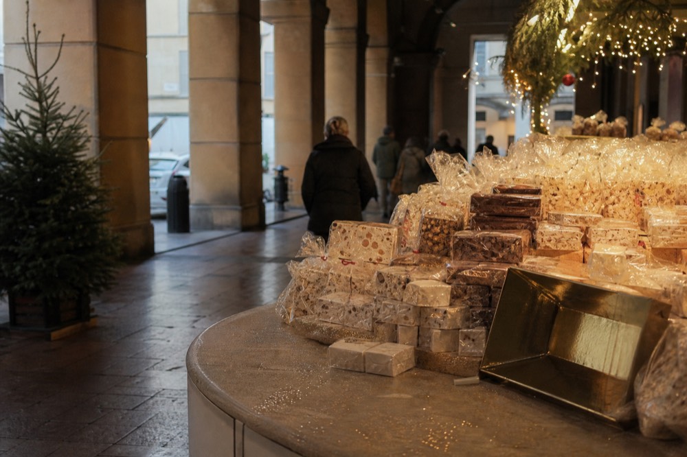 Festive market stalls stacked with wrapped sweets and seasonal goods under string lights