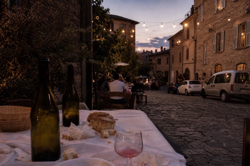 An outdoor festival table set with wine bottles and bread under string lights