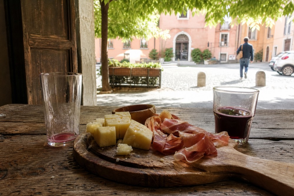 A tasting board with cheese cubes, prosciutto and small glasses of red wine on a wooden table