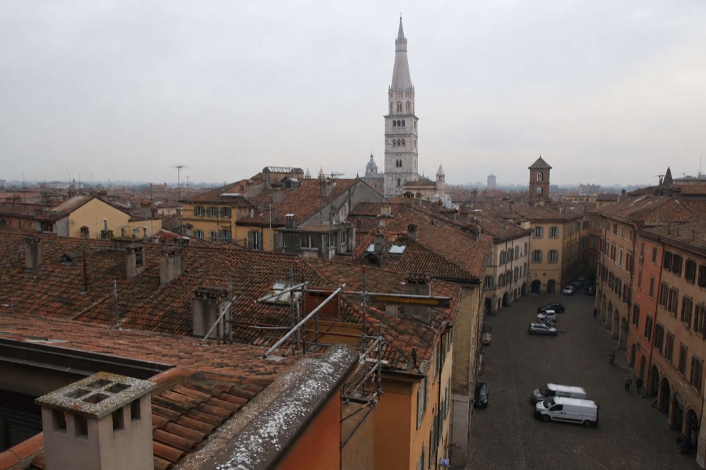 A cobbled square with a tall brick bell tower rising above rooftops
