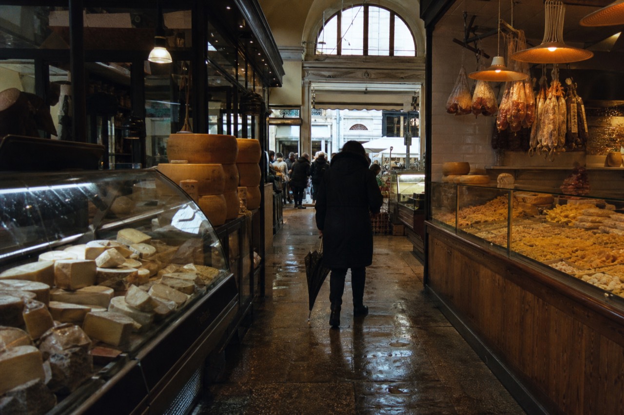 A covered food market hall with stalls of cheese, cured meats and fresh pasta under warm lights