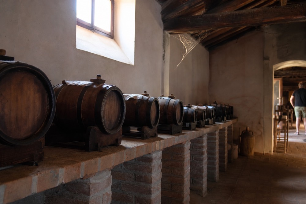 A sequence of small wooden barrels of different sizes inside a dim acetaia loft