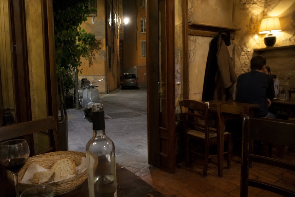 A trattoria interior with wooden tables, tiled floor and warm lamplight