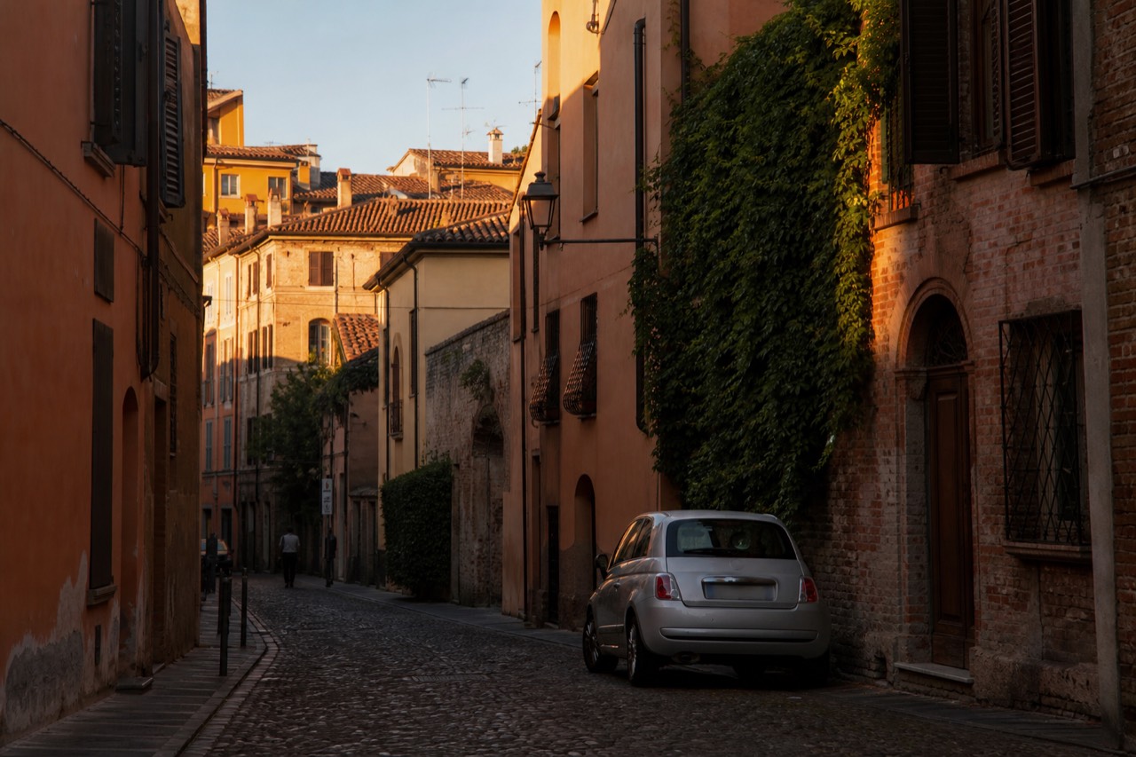 A quiet cobbled street in central Modena with historic brick buildings in warm evening light