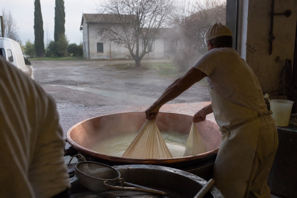 A cheesemaker lifting curd from a copper vat with a cloth