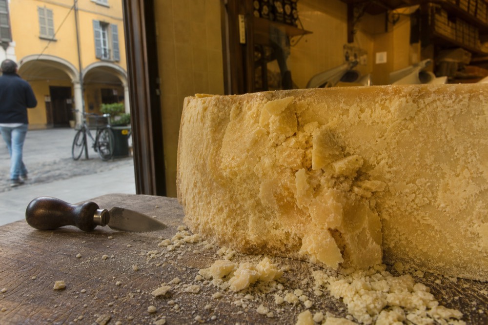 A cut piece of aged Parmigiano Reggiano showing its crumbly straw-coloured paste on a wooden counter