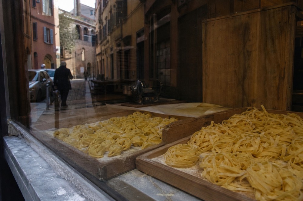 A display of fresh pasta shapes, tortellini and tagliatelle, inside a Modena shop window