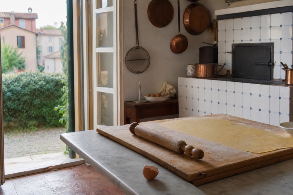 A pair of hands rolling pasta dough on a wooden board with a rolling pin in a Modena kitchen