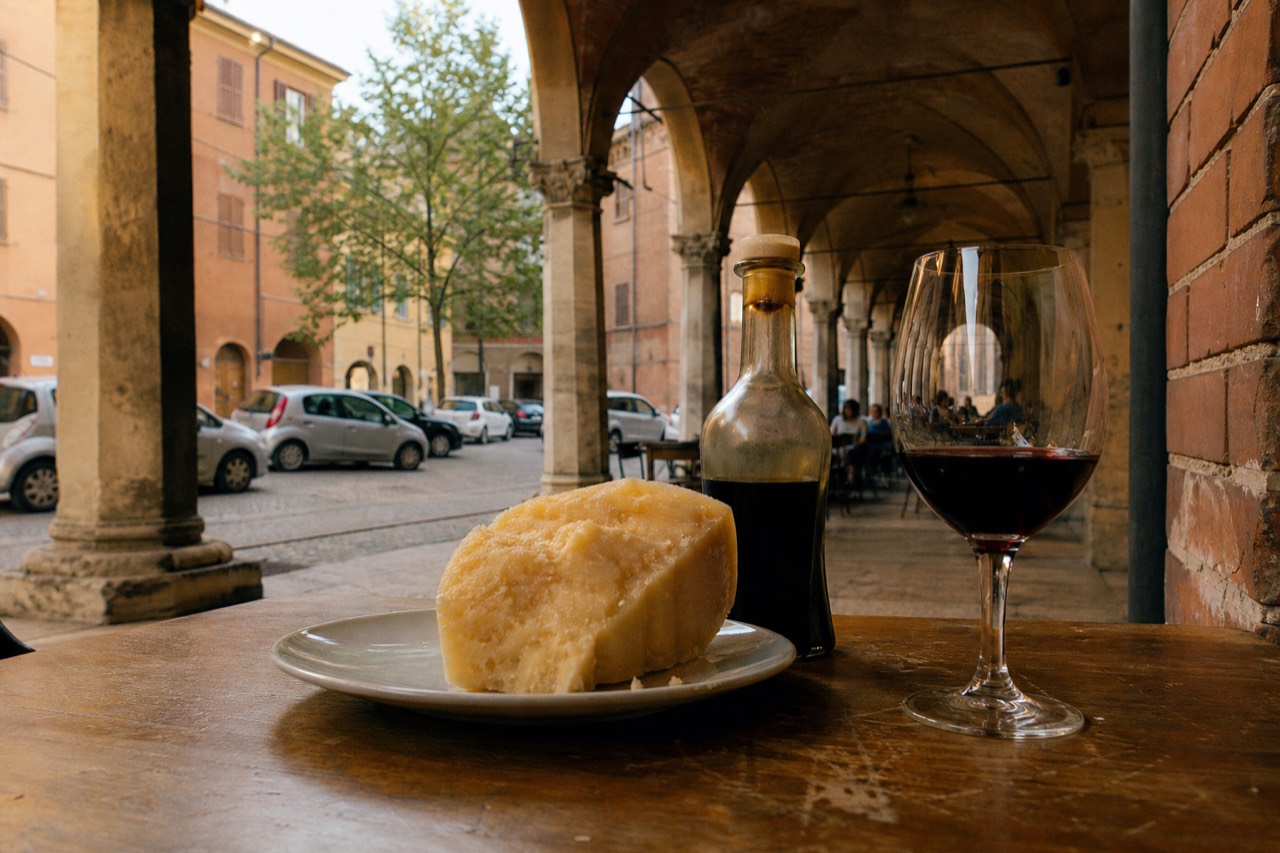 A table spread with Parmigiano Reggiano, traditional balsamic vinegar, and a glass of Lambrusco