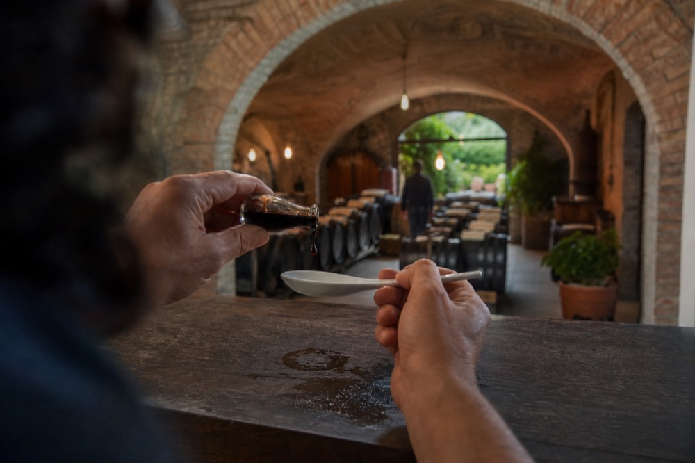 A producer pouring a drop of aged traditional balsamic from a small glass dispenser