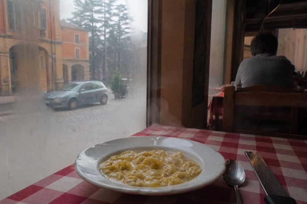 A bowl of handmade tortellini in golden capon broth on a checkered tablecloth