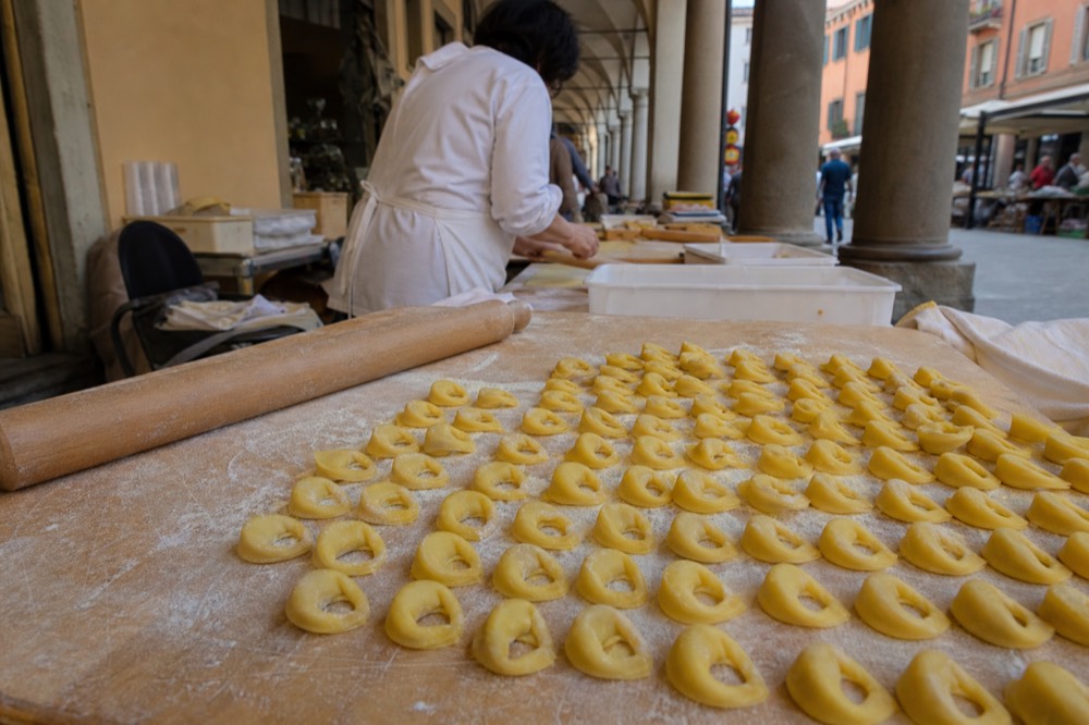 Hands folding small tortellini rings on a floured wooden board