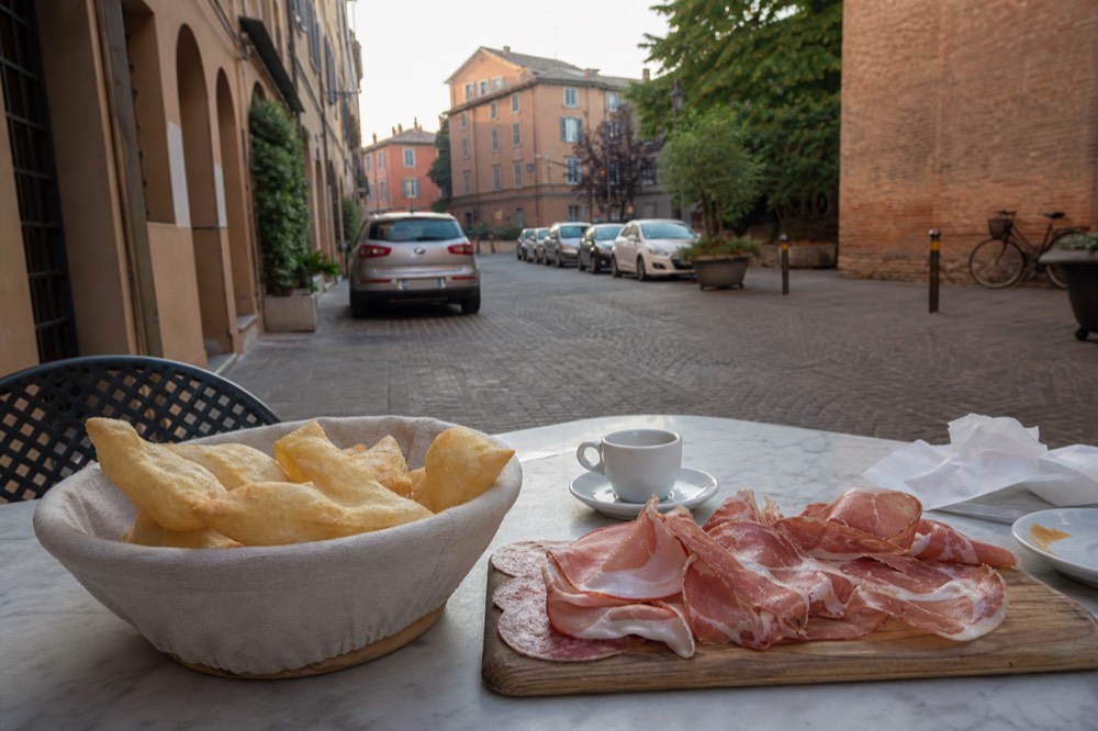 A basket of warm gnocco fritto beside a wooden board of cured meats