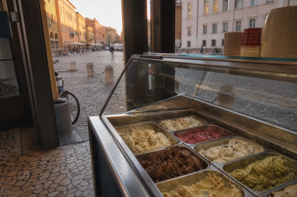 A gelato counter with rows of tubs inside a small Modena shop
