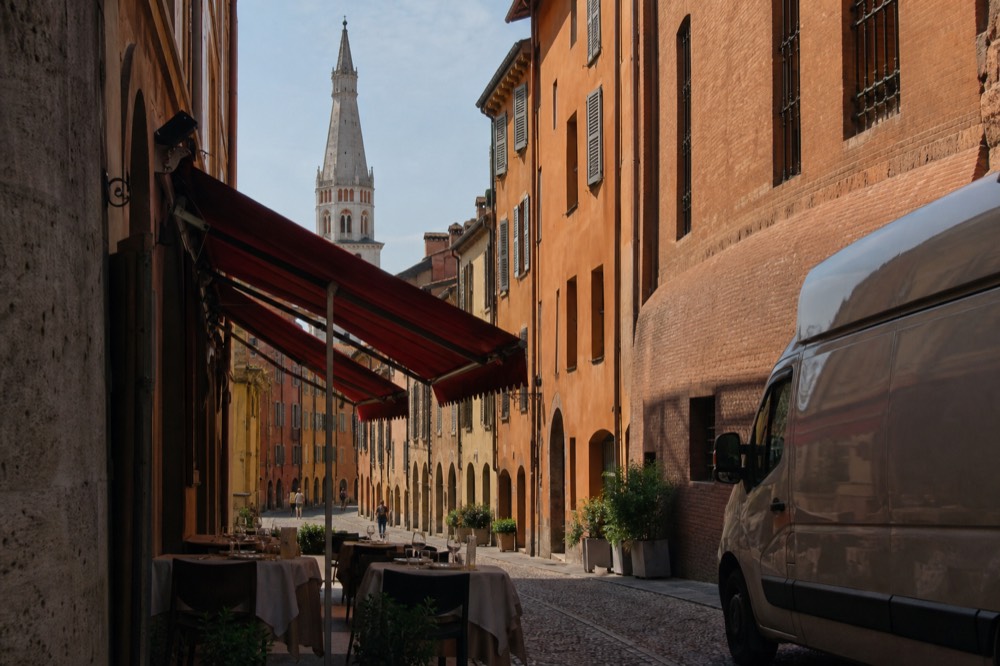 Red awnings above a cobbled Modena street with tables set for lunch