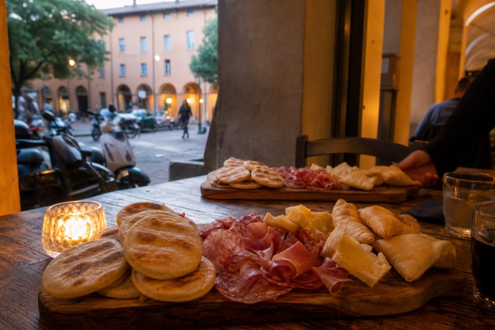 Plates of tigelle and gnocco fritto with salumi and cheese on a wooden board